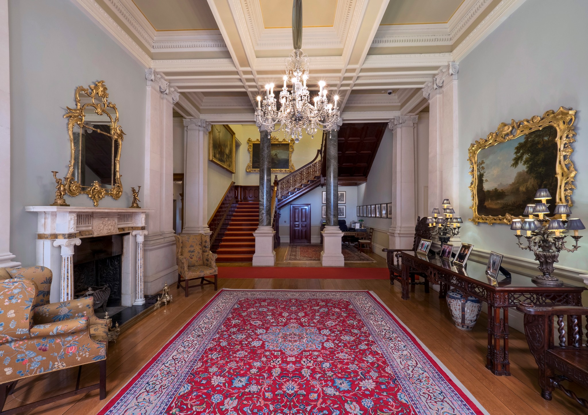 Farmleigh entrance hall featuring Connemara Marble pillars, Persian rug, Bohemian crystal chandelier, compartmentalised ceiling and 19th century furniture.