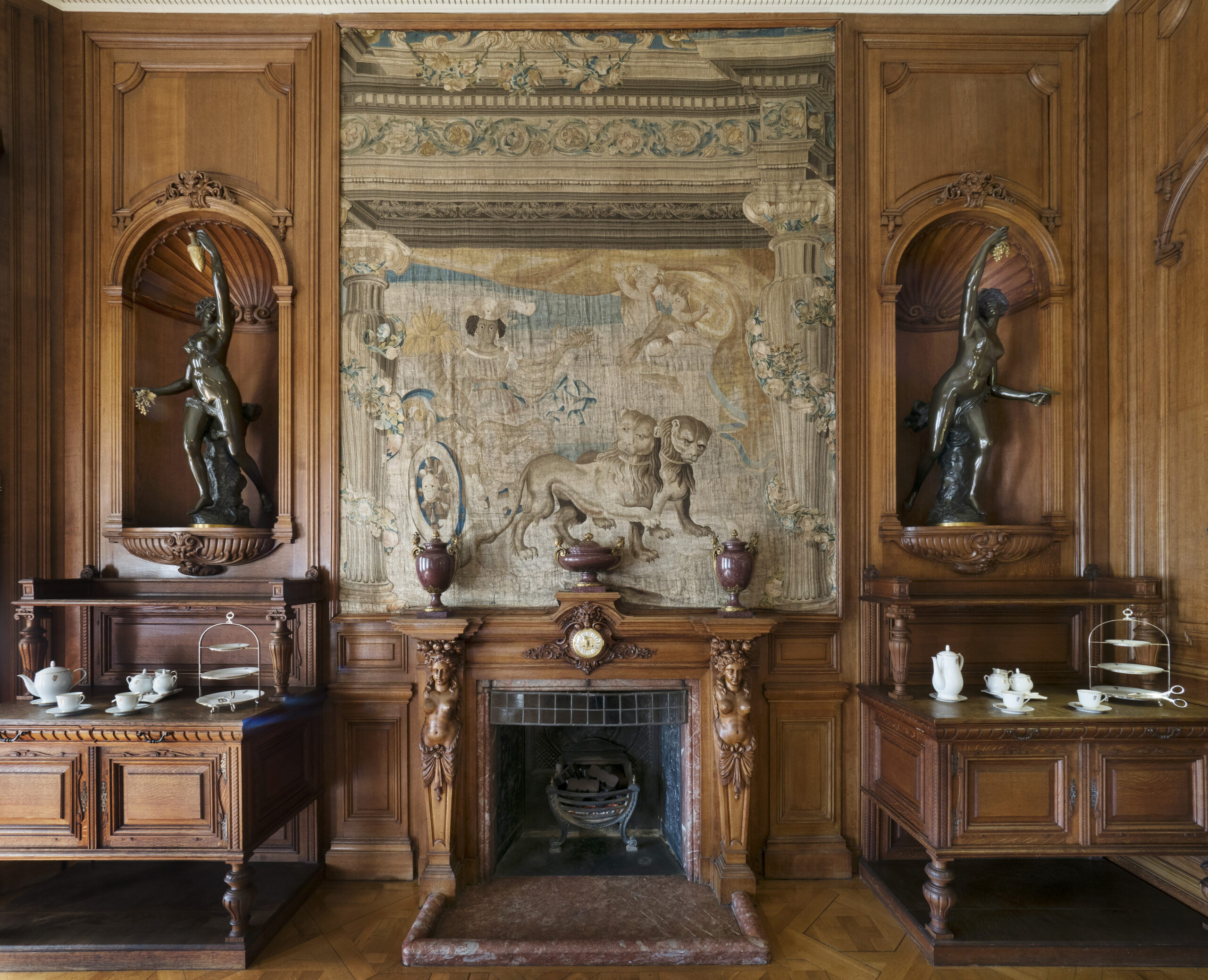 Wooden fireplace below tapestry featuring personification of Africa; lady in carriage pulled by lions