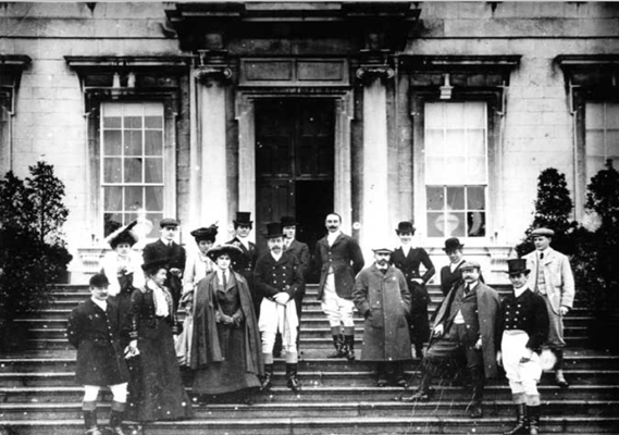 b & w photo of staff standing on steps at entrance to a big house